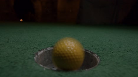 una mini pelota de golf amarilla cae en el hoyo de golf y rebota en el bolsillo de un campo