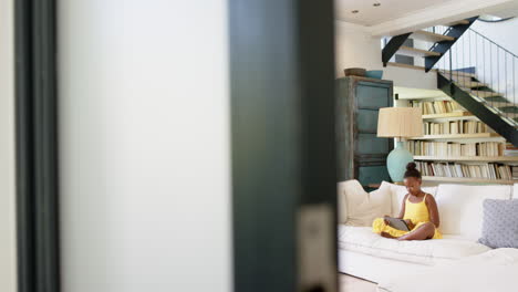 sitting on couch, girl using tablet in cozy living room with bookshelves, copy space