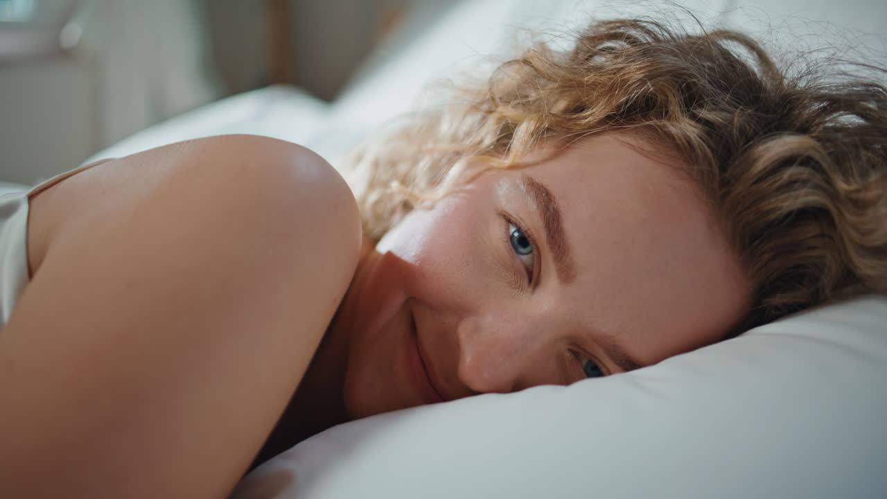 Closeup woman smiling pillow resting. Smiling curly girl bask in morning light