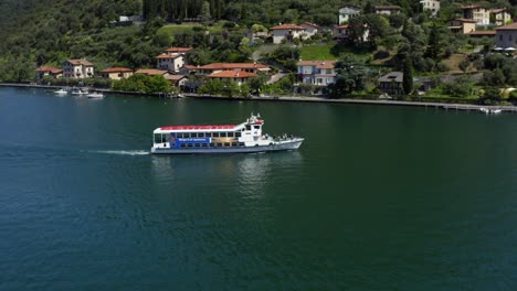 ferry boat with passenger cruising in the lake iseo passing by the town houses in lombardy, italy