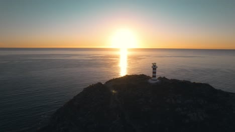Aerial-Slowly-ascending-reveal-beacon-light-on-hill-over-scenic-sunrise-at-ocean,-Cabo-San-Lucas