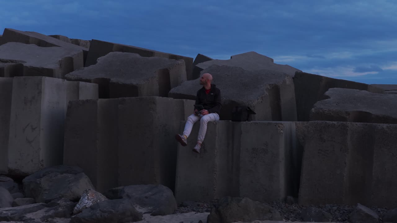 Man sits alone on large concrete breakwater blocks at dusk, Madeira, Portugal