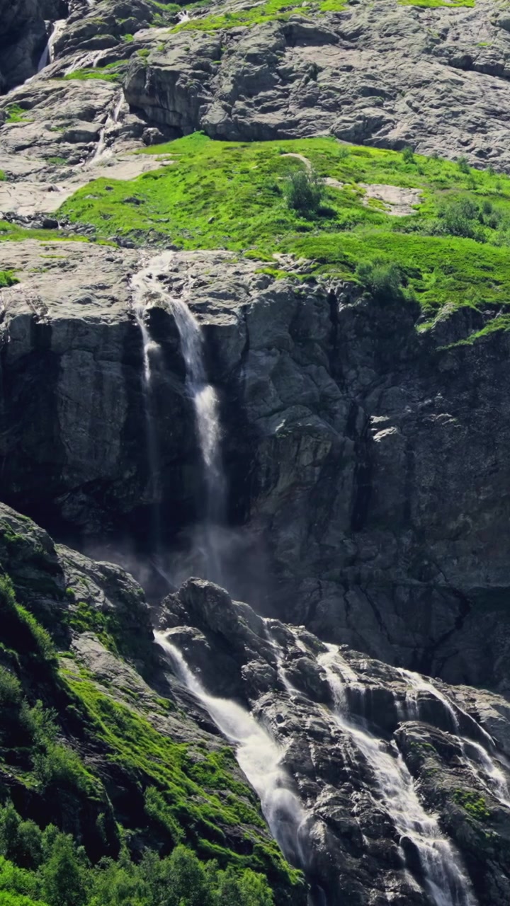 Potente cascata che scende da una montagna rocciosa con pendii verdi