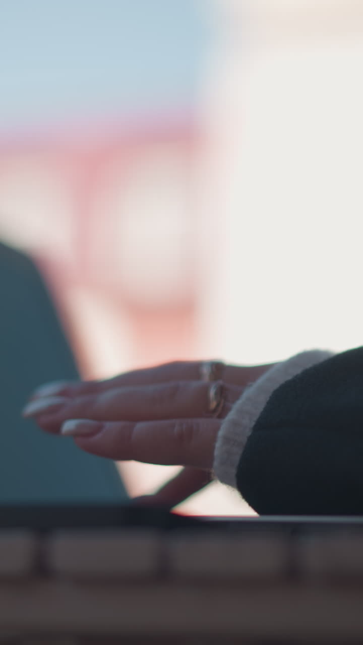 primer plano de manos escribiendo en un teclado de portátil adornado con anillos de plata y clavos pulidos, colocado en una mesa de madera con un teléfono inteligente cerca, con un fondo borroso