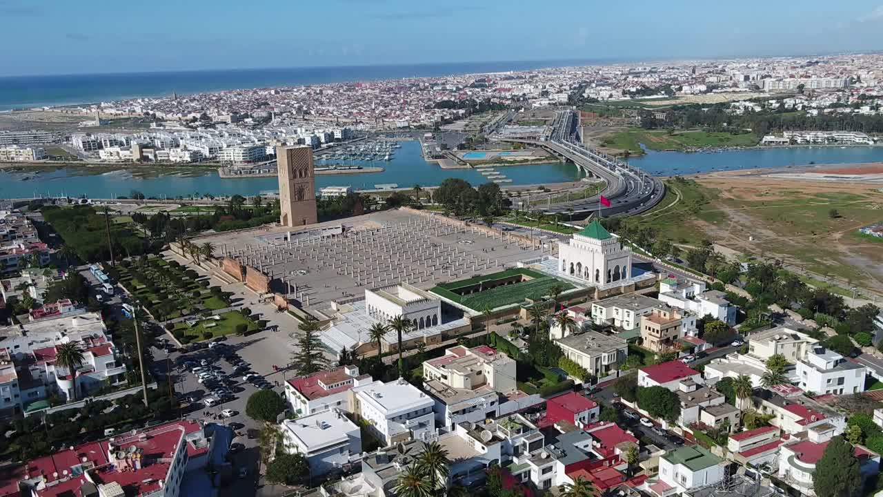 Comprehensive drone shot capturing Rabat's urban evolution. Features the historic Hassan Tower complex alongside the modern Hassan II Bridge connecting to Salé across the Bou Regreg river