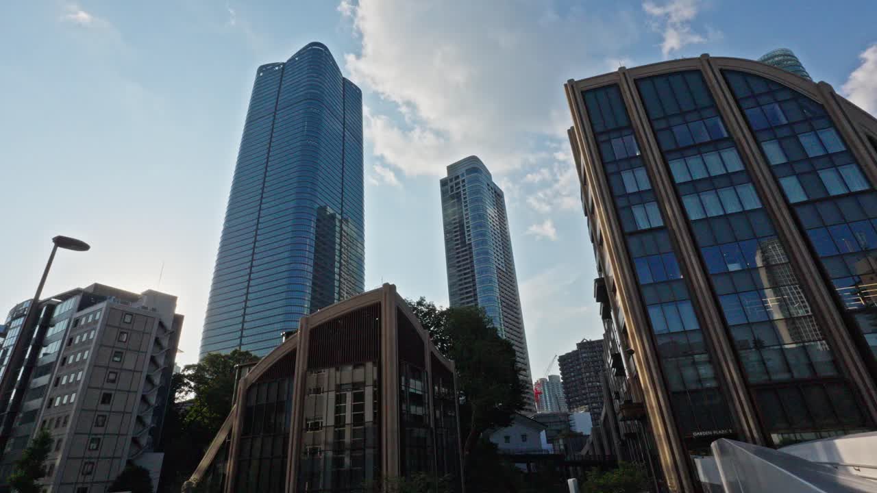 Low-angle view of soaring modern skyscrapers and unique architecture in Tokyo's Toranomon district. Buildings stand prominently against a bright, cloudy sky.