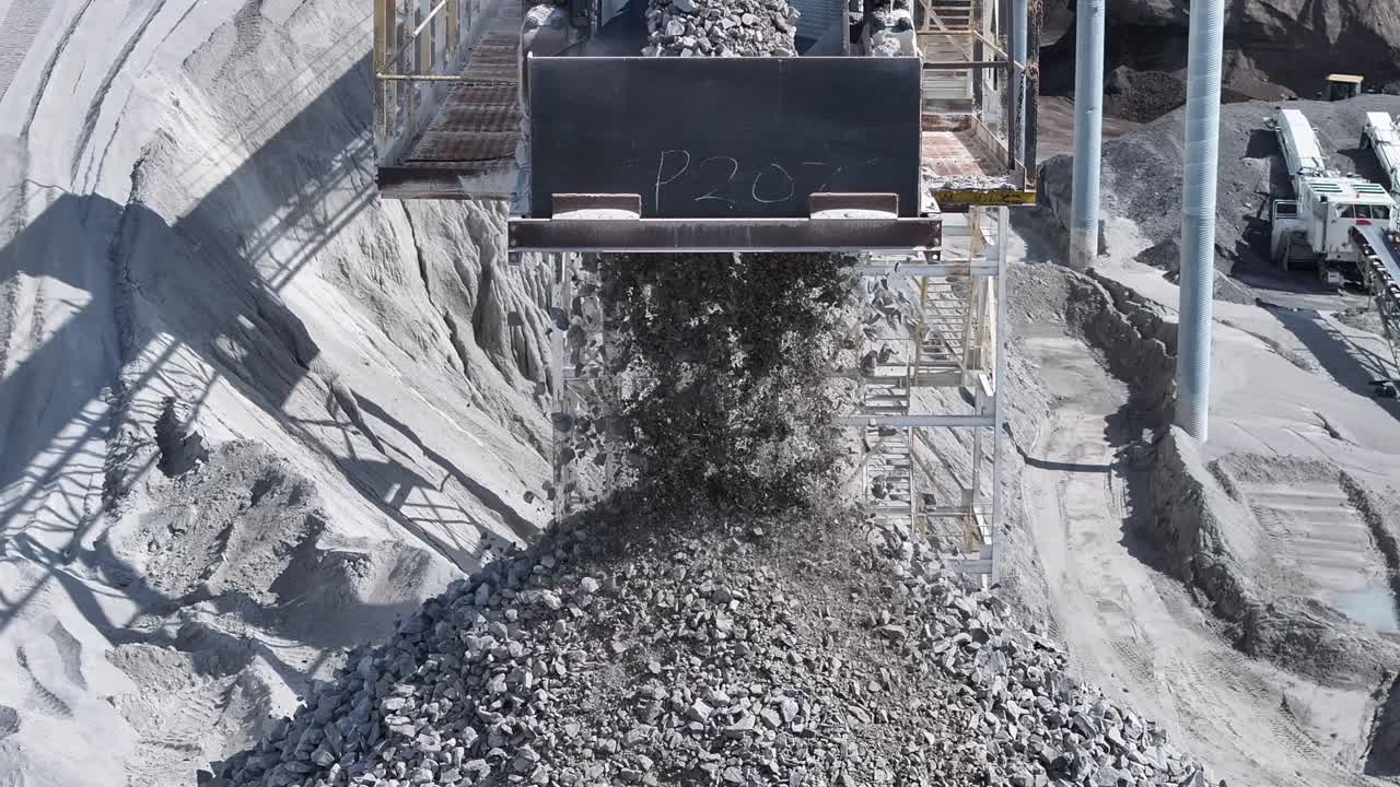 Slow motion footage of gravel falling off a conveyor belt into a big pile in a quarry.