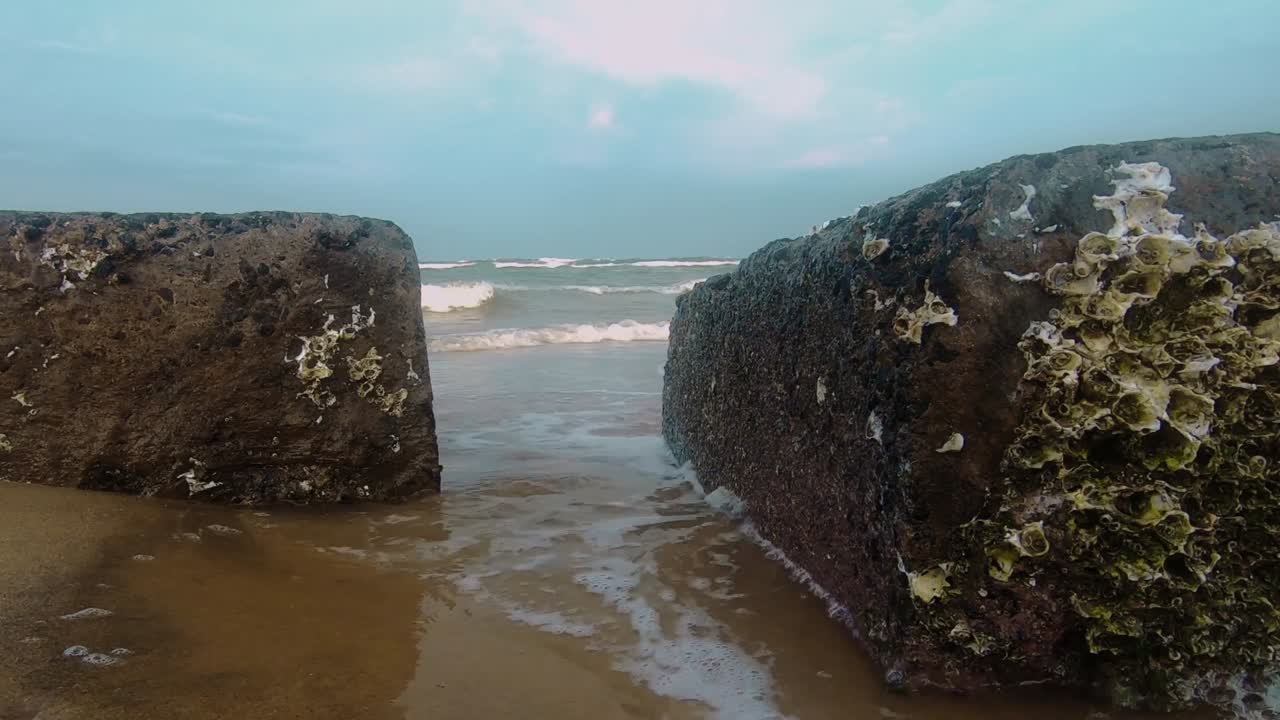 Looking at sea between rocks on beach on cloudy day. Static