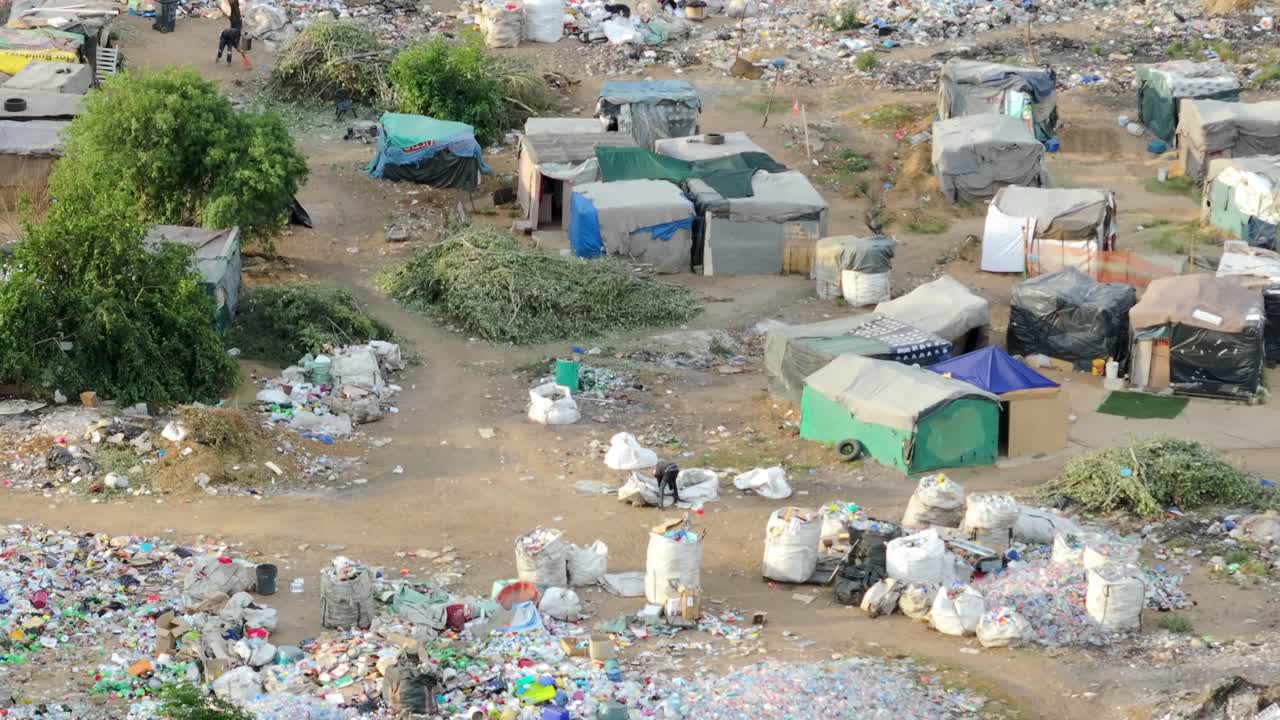 Ariel shot revealing a community living in a large garbage area, where makeshift shelters provide living spaces for poor people