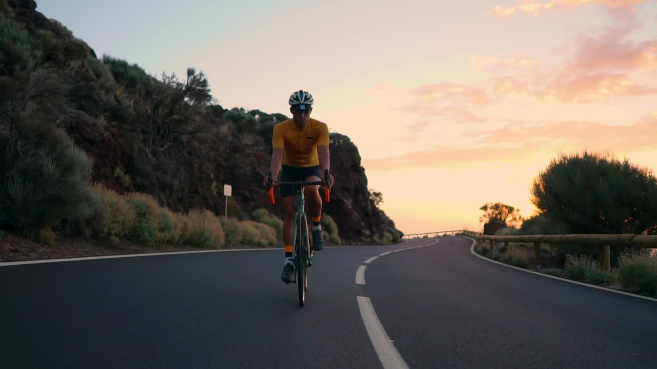 The athlete on a bike is captured in slow motion riding a mountain serpentine, enjoying the island's view, embodying dedication to a healthy lifestyle at sunset