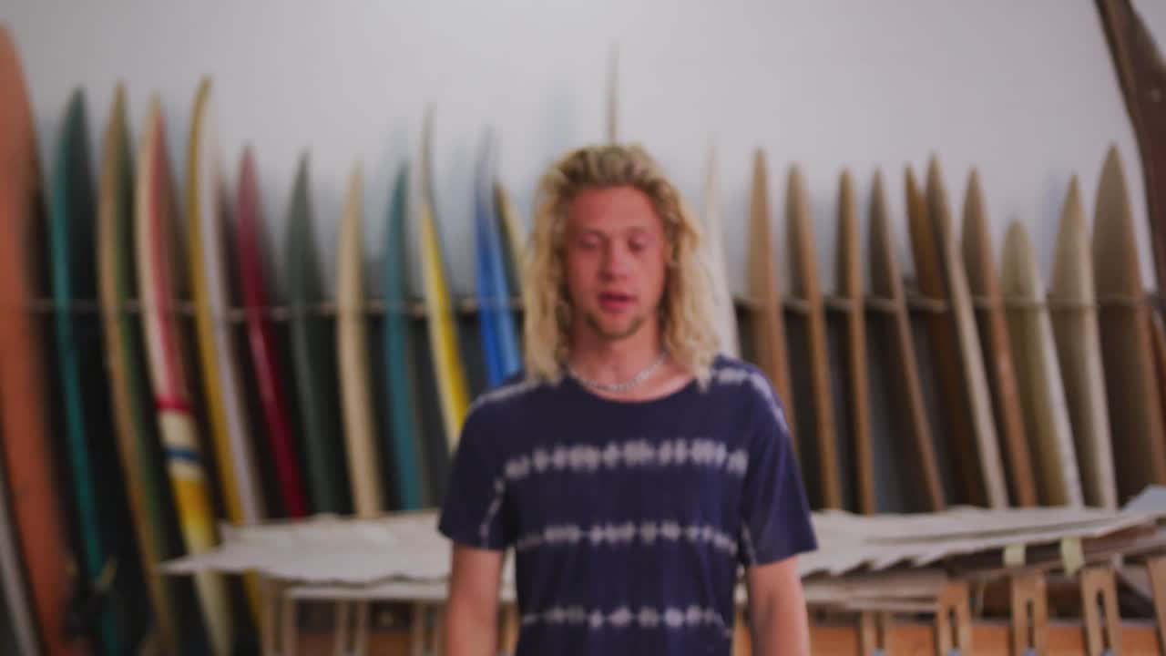 hombre caucásico fabricante de tabla de surf en su estudio con tablas de surf en un rack en el fondo