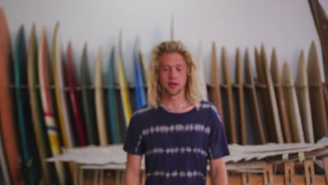 Caucasian-male-surfboard-maker-in-his-studio-with-surfboards-in-a-rack-in-background