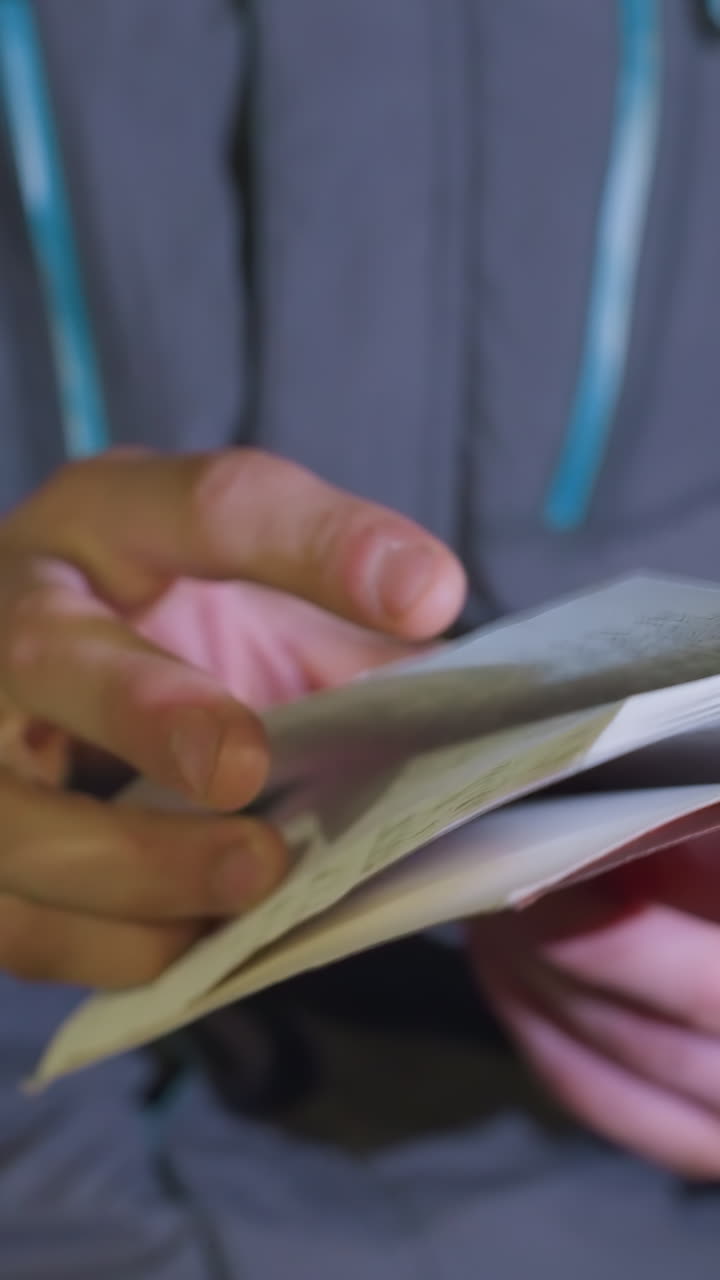 vista de mano de primer plano de un hombre volviendo la portada roja del libro al aire libre por la noche con efecto bokeh borroso de las luces de los automóviles que pasan, iluminado por las luces urbanas de la ciudad