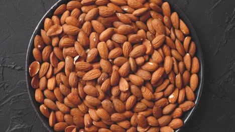 nueces enteras de almendras en un plato negro colocado sobre una mesa de piedra negra