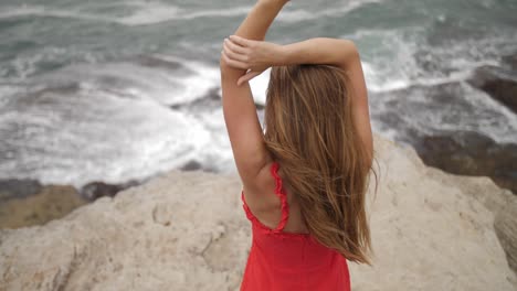 chica sexy en vestido rojo cóctel de pie sobre las rocas y mirando las olas del mar con las manos en la cabeza - suburbios del este, nueva gales del sur, australia