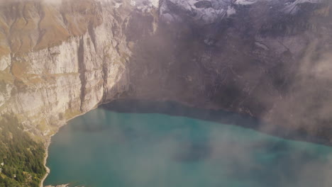 Aerial-View-Through-Clouds-of-Mountainside-Oeschinen-Lake-in-Switzerland-Alps-Region,-Oeschinensee-Lake-Scenery