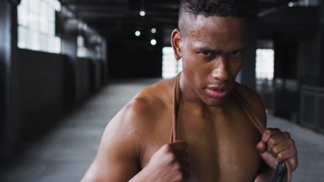 hombre afroamericano sin camisa cansado después de saltar la cuerda en un edificio urbano vacío