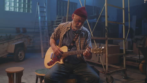 older man playing acoustic guitar in a warehouse