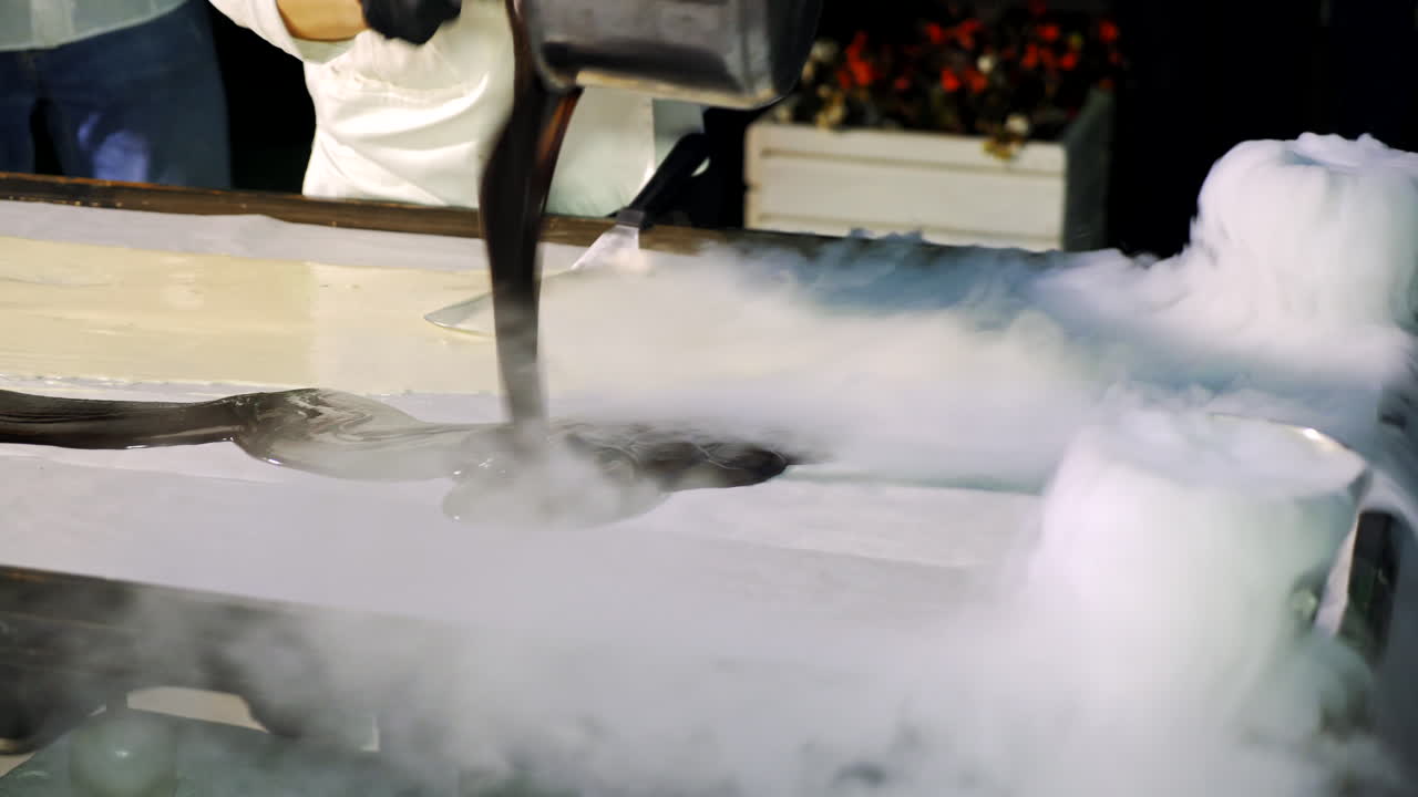 Chief cook makes delicious black and white ice-cream on a big table. Modern preparation of ice-cream on the white surface with liquid nitrogen.
