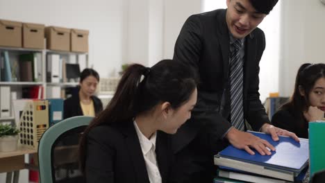 closeup of japanese male boss giving a heavy stack of documents to his worker. tired woman employee overwhelmed by the assignment in the workplace