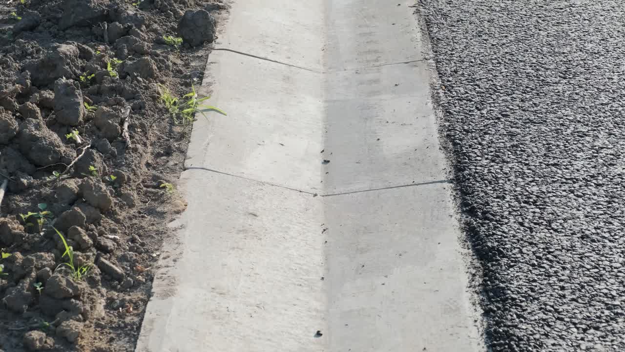 Asphalt road with stormwater on the side of the road with a ditch for water and a glade of green lawn along the road.