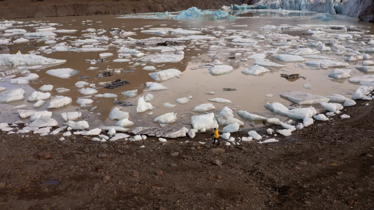 аэросъемка: боковая съемка одного человека, идущего по берегу лагуны ледника свинафеллсйокудль в исландии