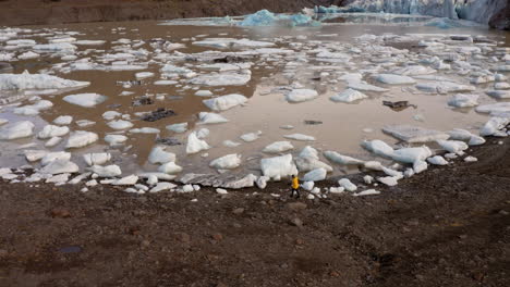 antena: seguimiento lateral de un hombre caminando por la orilla de la laguna glaciar svinafellsjokull en islandia
