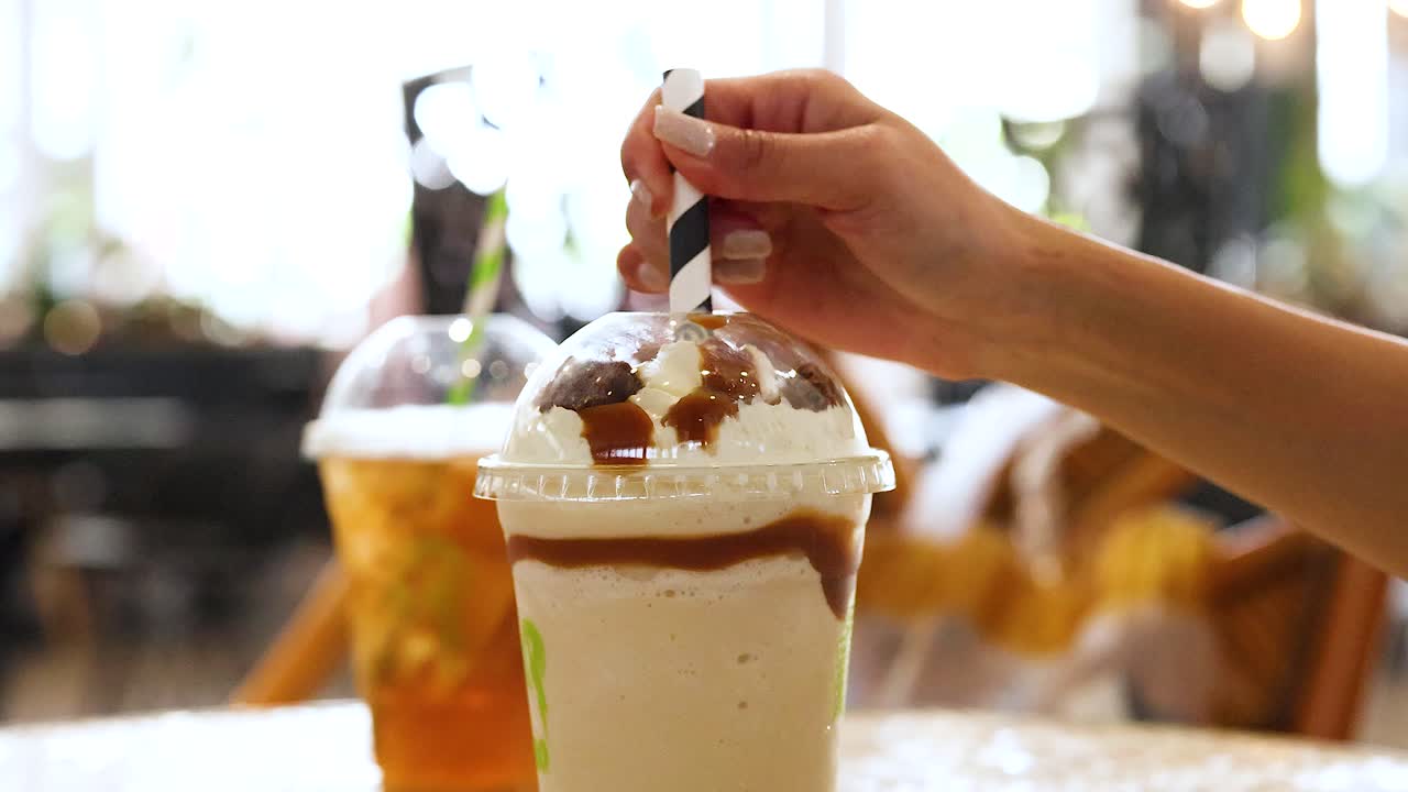 A hand stirs a creamy drink topped with caramel, set against a bright cafe background in Gold Coast, Australia