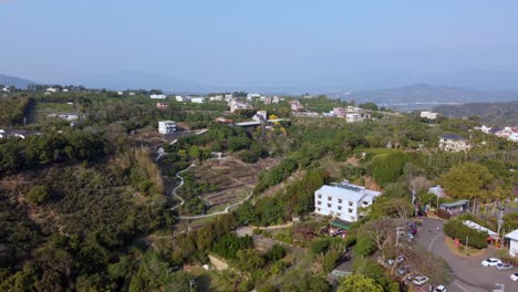 A-lush-hillside-community-with-homes-and-greenery,-under-a-clear-sky,-daylight,-aerial-view