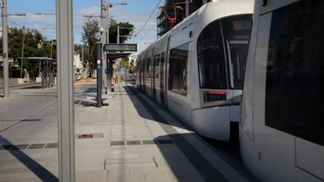 Tram-arriving-at-the-light-rail-platform-with-cyclist-passing-by,-establishing-shot