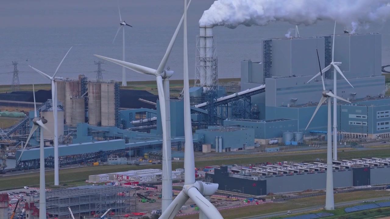 Aerial view showing the contrast between renewable energy from a wind farm and a traditional industrial power plant emitting smoke