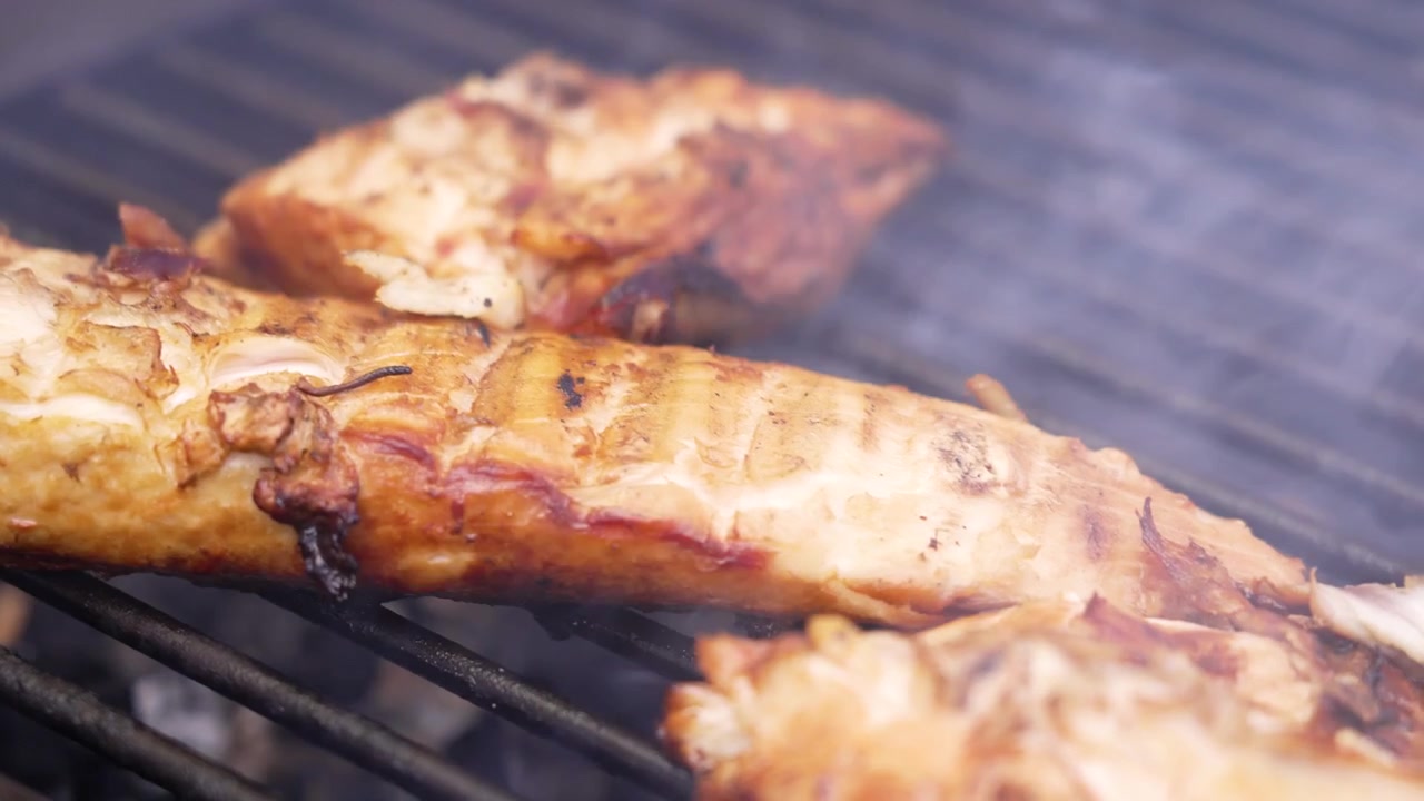 Primo piano di filetti di pesce conditi che cuociono su un barbecue fumante durante un picnic estivo