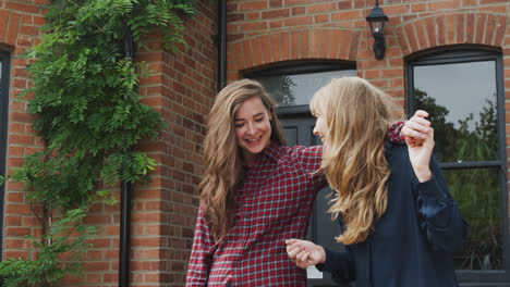 portrait of excited gay female couple standing outside new home holding keys together