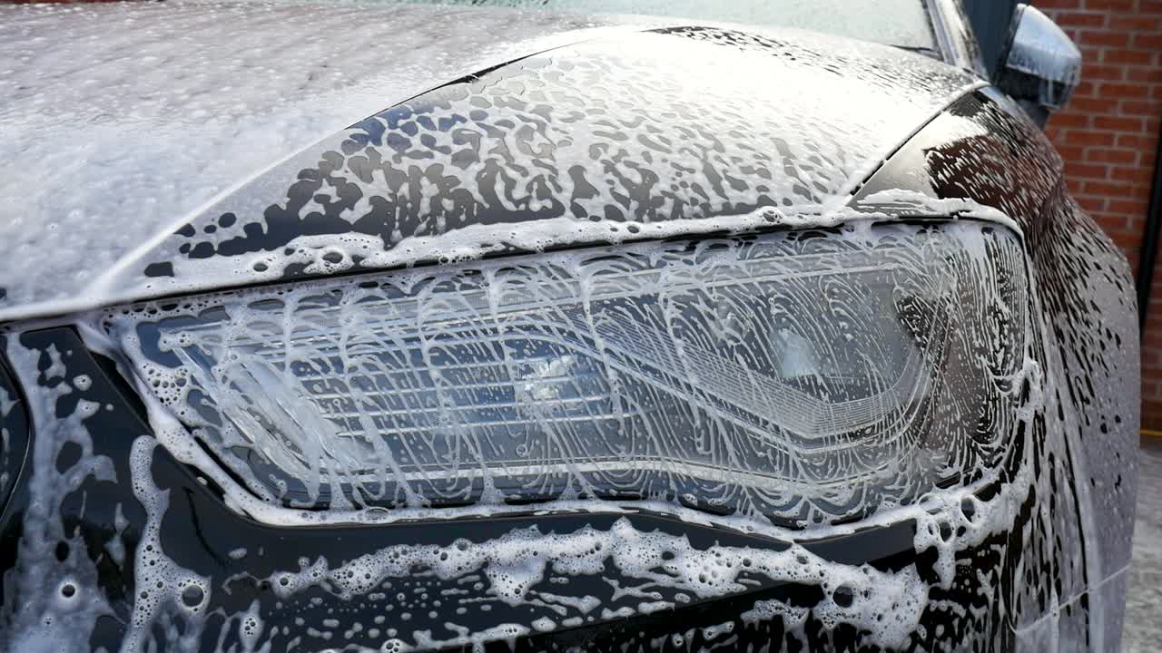 Faro dell'auto immerso nello shampoo e nelle bolle dopo la pulizia.