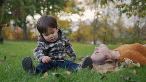 una madre feliz y su hijo juegan juntos, se acuestan en la hierba en el parque. un niño asiático ríe felizmente