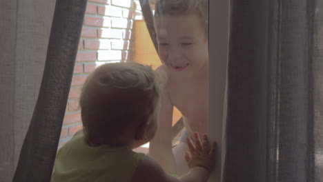 hermano y hermana pequeña mirándose por la ventana