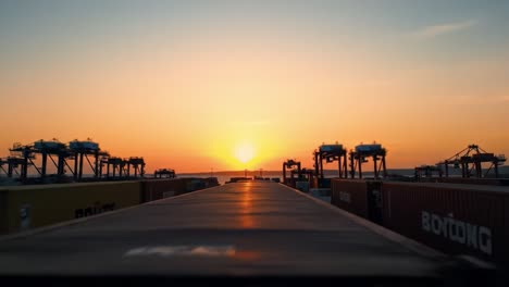 breathtaking sunset viewed from the port with cargo containers lined up, showcasing bustling shipping operations in the background and vibrant colors in the sky.