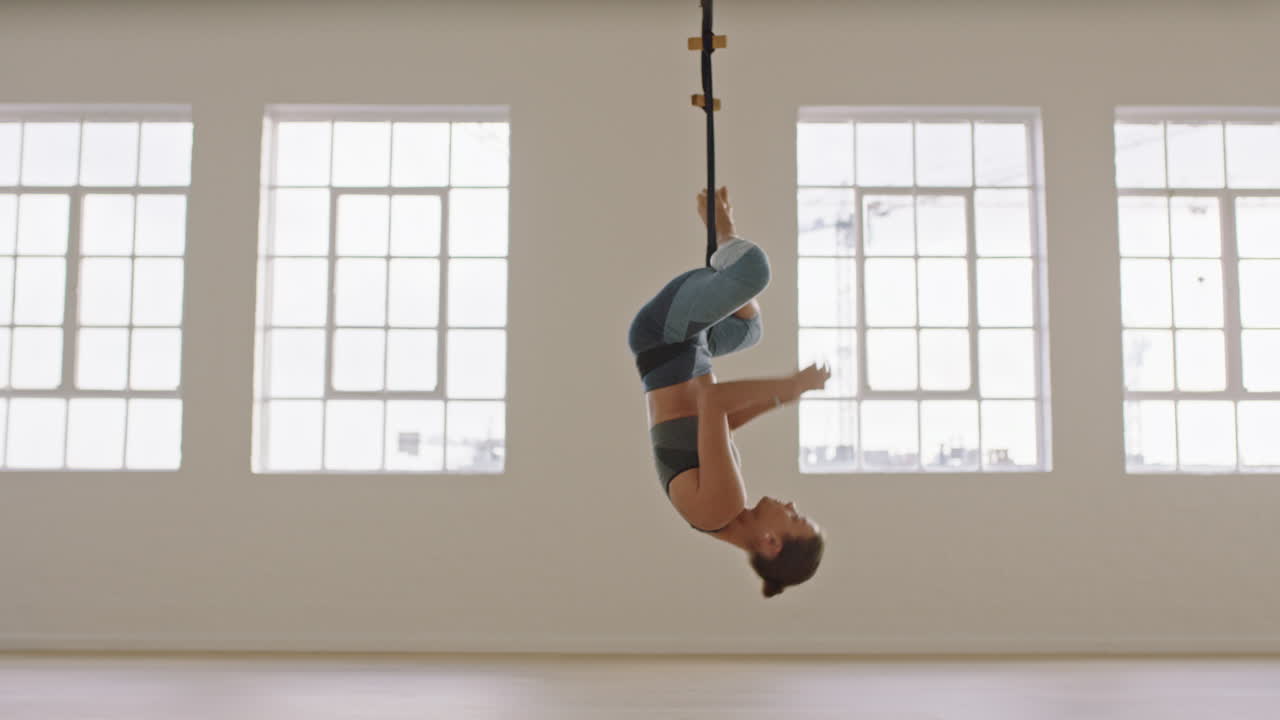 aerial yoga woman practicing inverted butterfly pose hanging upside down using hammock enjoying healthy fitness lifestyle exercising in studio training meditation at sunrise
