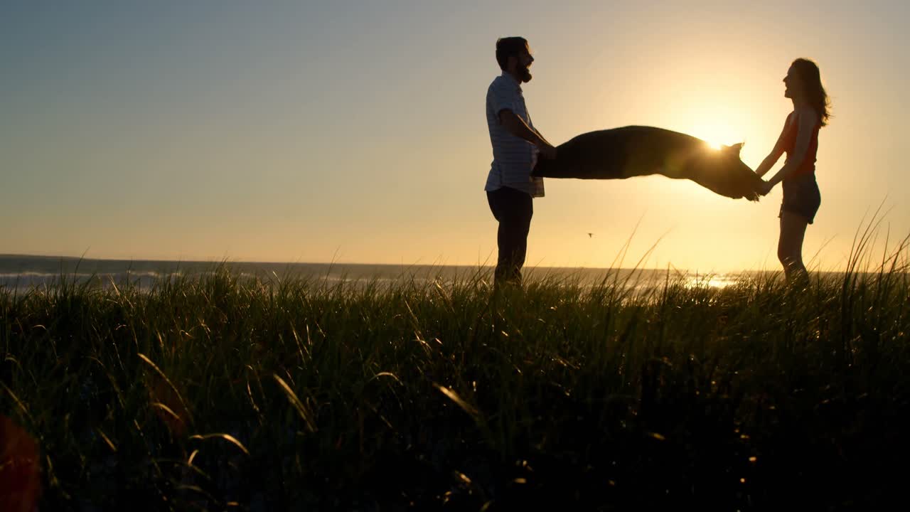 해변 4k에서 피크닉 담요를 흔드는 젊은 부부의 실루 ⁇