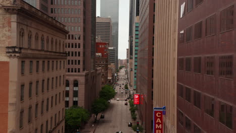 Drone-flying-along-Elm-street-between-tall-commercial-buildings.-Elevated-view-of-downtown-road-with-traffic.-Dallas,-Texas,-US