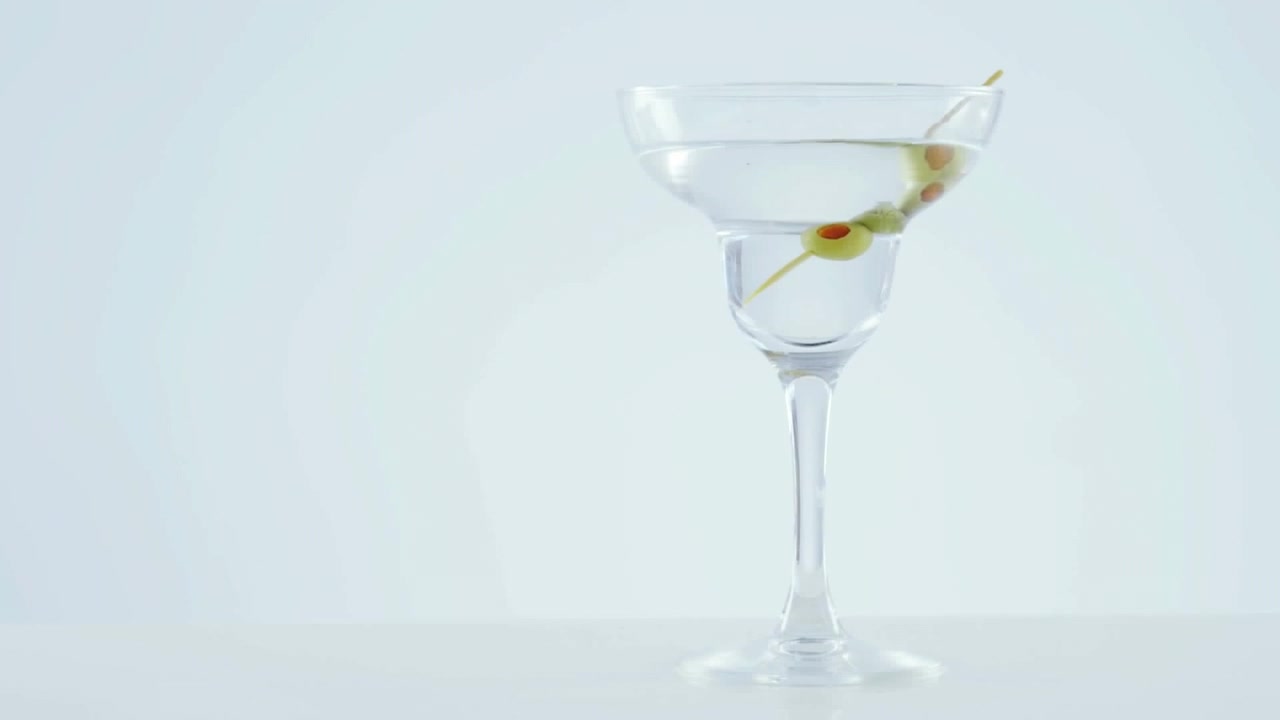 Carta grigia che brucia su olive in un bicchiere da cocktail su sfondo grigio