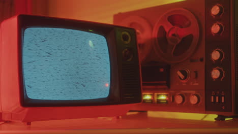 vintage tv set and reel-to-reel tape recorder in studio with neon light