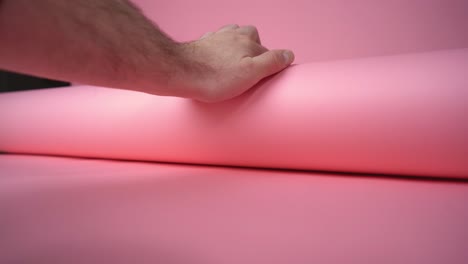 hand unrolling pink background paper for a photo and video shoot and rolling over camera - still shot