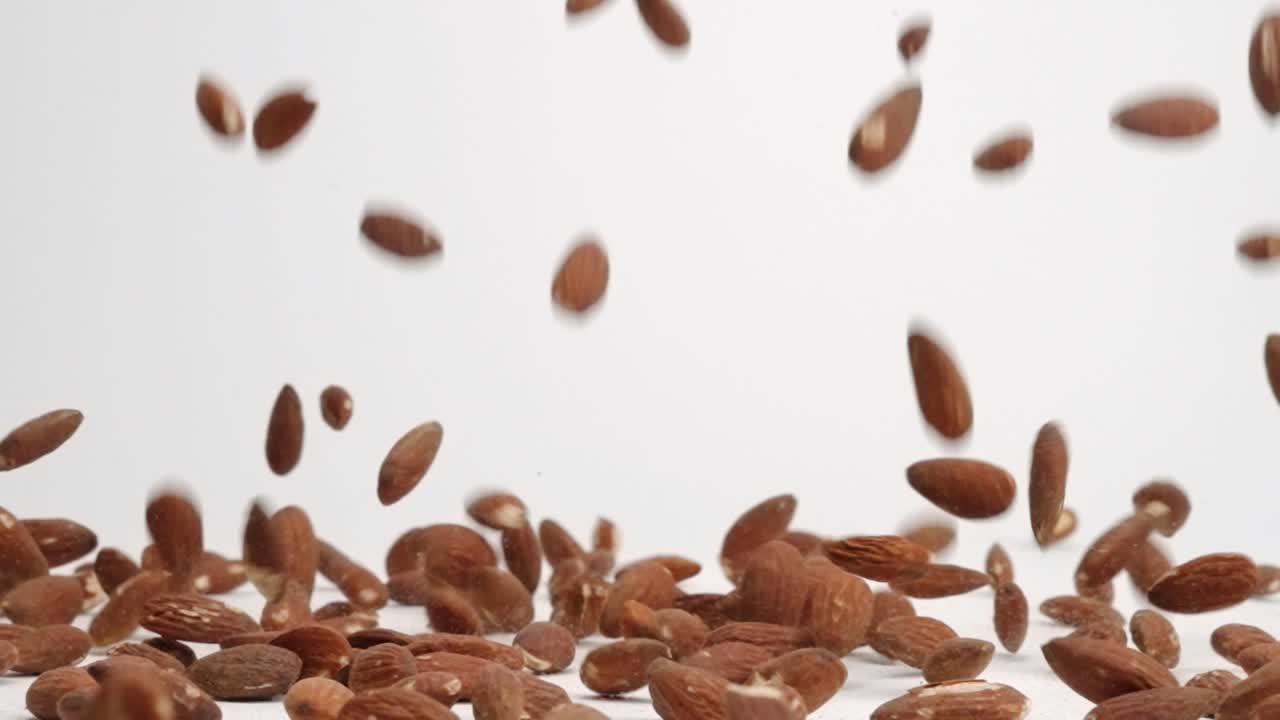 Whole raw almonds bouncing and falling into pile on white table top in slow motion