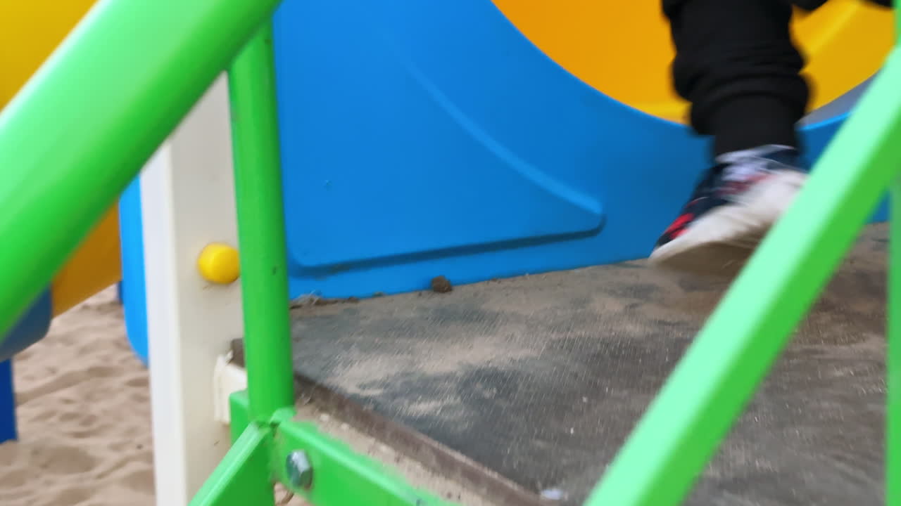 Little child's feet go up by the stairs. Unrecognized kid climbs the steps on the playground.