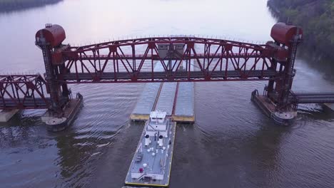 a beautiful aerial of a barge traveling on the mississippi river under a large steel drawbridge