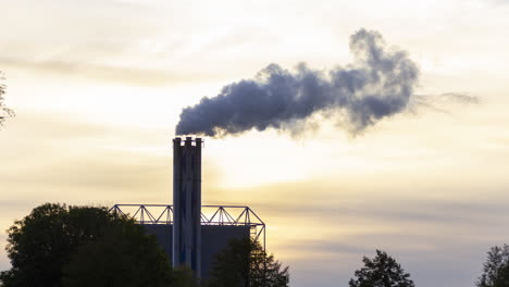 time lapse of smoking factory chimney against the background of a setting sun - slow zoom in