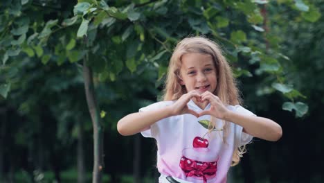 playful cheerful child waves his hand. portrait of a little girl in the park. human emotions. figures and gestures with fingers