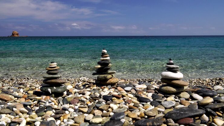 Tre torri di rocce Zen impilate su una spiaggia con acqua cristallina sullo sfondo in Sardegna, Italia.