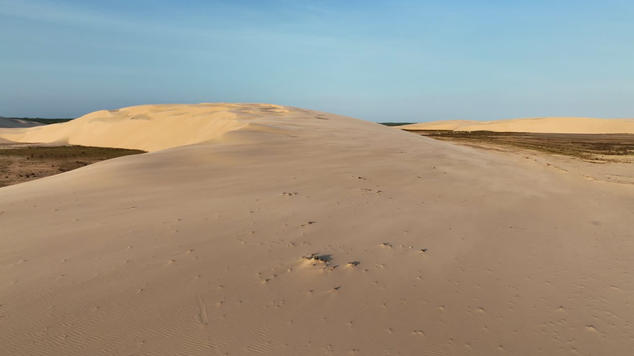 Expansive sand dunes with scattered dry vegetation near the Parnaíba River in Araioses, Maranhão, Brazil. Backward aerial view.